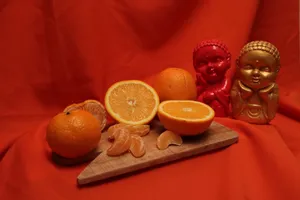 Colorful Buddha statues alongside fresh oranges on a wooden tray against a red backdrop. jigsaw puzzle