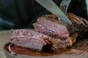 person slicing juicy medium rare meat on top of brown wooden cutting board jigsaw puzzle