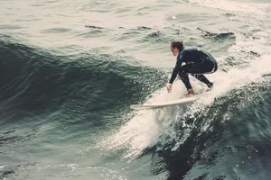 man in black wet suit riding white surfboard on sea during daytime jigsaw puzzle