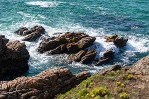 Stunning view of a rocky coastline with ocean waves crashing onto the shore under a bright sky. jigsaw puzzle