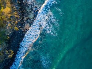 A breathtaking aerial view showcasing turquoise ocean waves crashing against a rocky shoreline. jigsaw puzzle