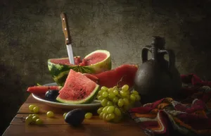 A rustic still life composition featuring watermelon, grapes, plums, and tableware on a wooden table. jigsaw puzzle