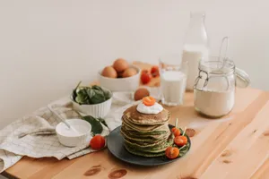 Delicious stack of pancakes with fresh spinach, tomatoes, eggs, milk, and yogurt on a wooden table. jigsaw puzzle