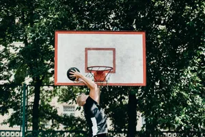 A man performing a slam dunk on an outdoor basketball court amidst lush greenery. jigsaw puzzle