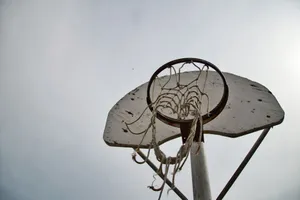 Low angle view of an old basketball hoop with worn net under a cloudy sky, emphasizing outdoor sports nostalgia. jigsaw puzzle