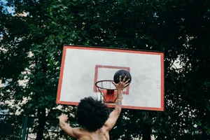 A man skillfully dunking a basketball in an outdoor court during daytime play. jigsaw puzzle