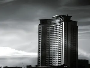 Tall modern skyscraper with reflective glass facade against a cloudy sky, captured outdoors during the day. jigsaw puzzle