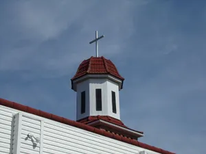 Low-angle view of a white chapel steeple with red roof and cross against a blue sky. jigsaw puzzle