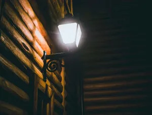 Charming vintage wall lamp on a wooden log cabin exterior at night, casting a warm glow. jigsaw puzzle