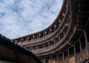 Curved wooden Chinese tulou featuring red lanterns under a blue sky. jigsaw puzzle
