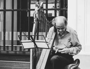 Black and white image of an elderly musician playing harp on the street. jigsaw puzzle