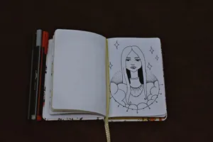 Artistic sketch of a woman in an open notebook with pens on a dark surface. jigsaw puzzle