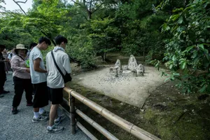 Tourists observe a small rock garden surrounded by lush greenery. jigsaw puzzle